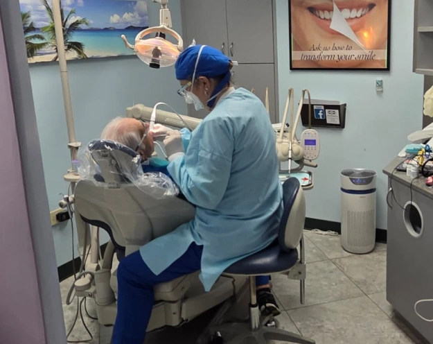 Dentist performing a dental cleaning and exam on a patient seated in a dental chair, wearing gloves and protective eyewear