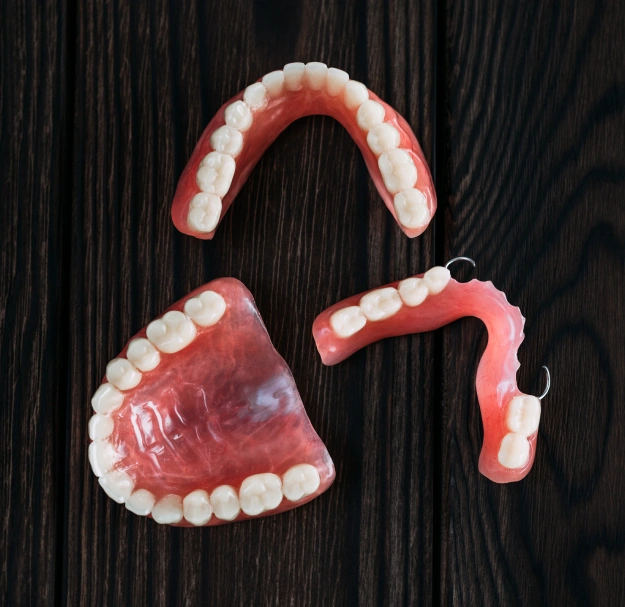 Full and partial dentures displayed on a dark wood surface, showing upper and lower arches with natural-looking teeth