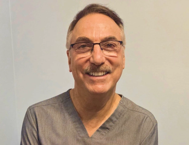 Portrait of Dr. Gary D. Levine, smiling dentist wearing glasses and gray scrubs