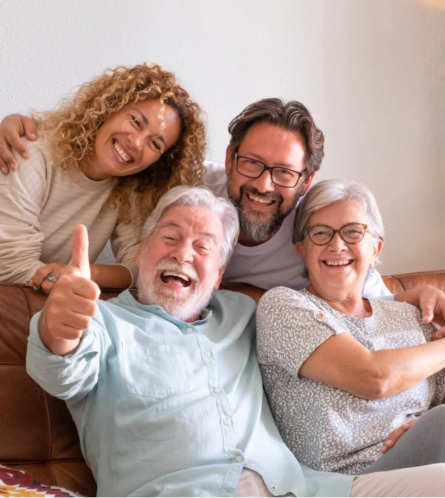 Multi-generational family smiling and laughing together on a couch, giving a thumbs up