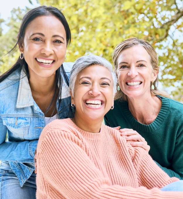 Three smiling women standing together outdoors, enjoying healthy smiles