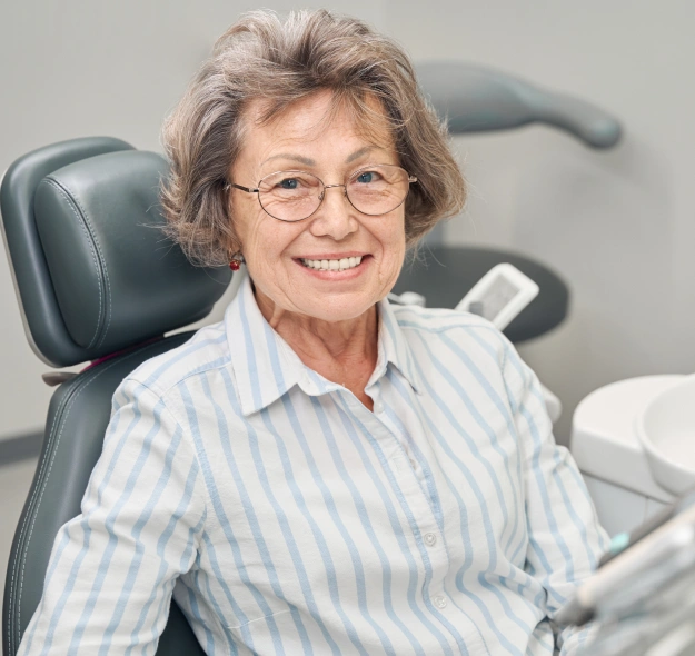 Smiling senior woman with glasses sitting in a dental chair before treatment