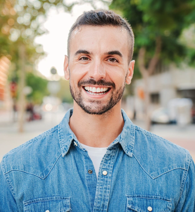 Smiling man with bright white teeth standing outdoors on a city street