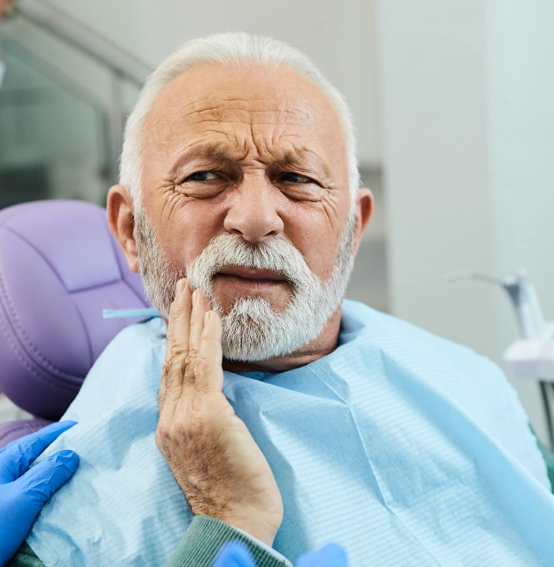 Senior man in a dental chair holding his cheek in discomfort from tooth pain