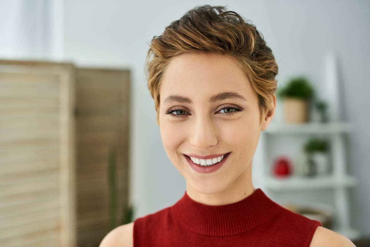 Smiling woman with healthy white teeth wearing red turtleneck in dental office.